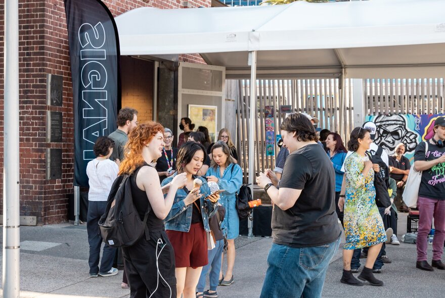 Young people milling about outside a red brick building with an attached white marquee structure.