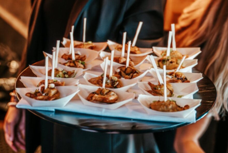 A person holding a tray of small canapes in individual serving portions.