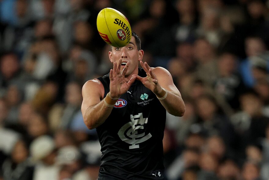 A Carlton AFL football player catching a yellow ball during a match.
