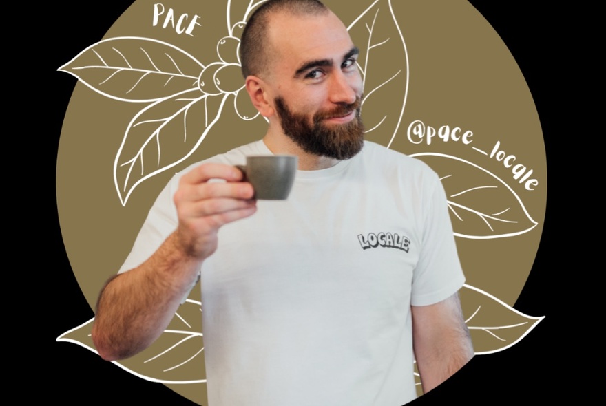 A smiling bearded man in a white t-shirt holding an espresso coffee cup in front of a drawing of coffee beans.