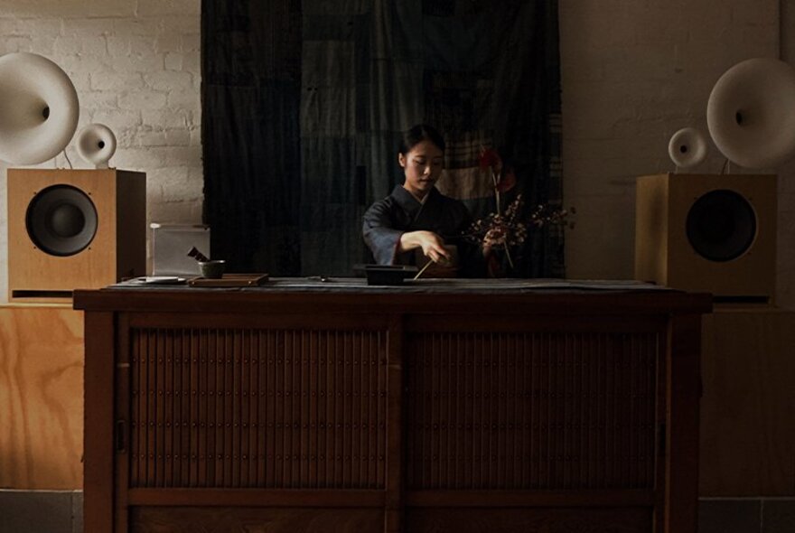 Woman working at a bench in a dark venue with wooden cabinets.