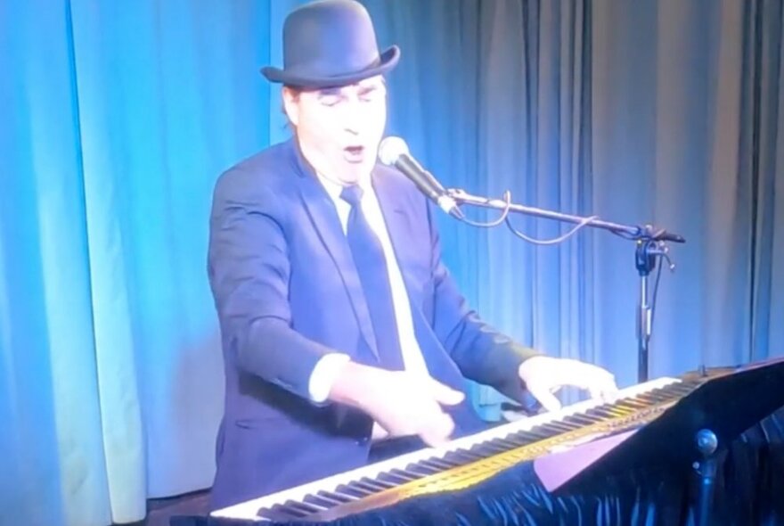 Pianist seated at a piano on stage in front of blue curtains.