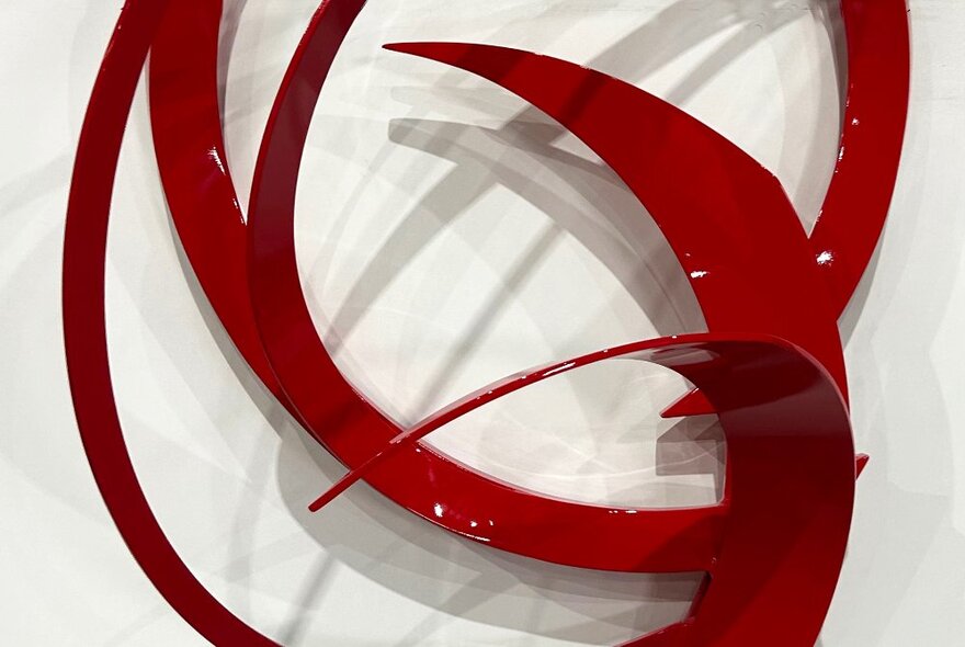 Artwork with red metal curves against a white background showing its shadow. 