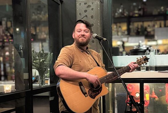 Man with a guitar smiling in front of a microphone at a restaurant
