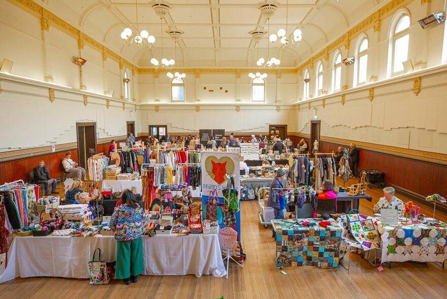 People browsing a colourful indoor makers market with quilts, knits, clothing and more.