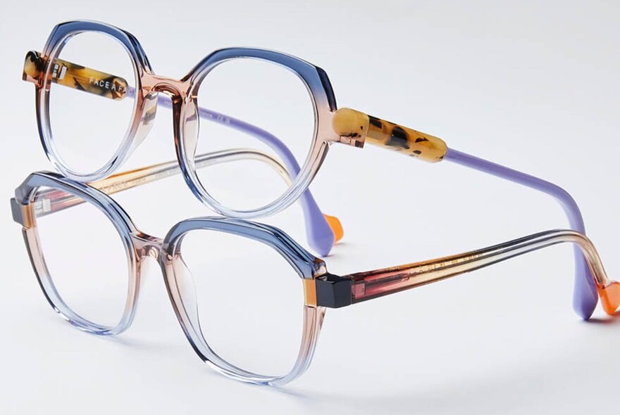 Two pairs of multi-coloured eye glasses, one balancing on the top of the other; white background.