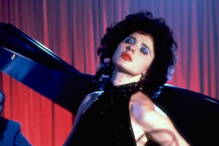 A still from the movie Blue Velvet showing Isabelle Rossellini as singer Dorothy Vallens, her eyes closed as she performs. 