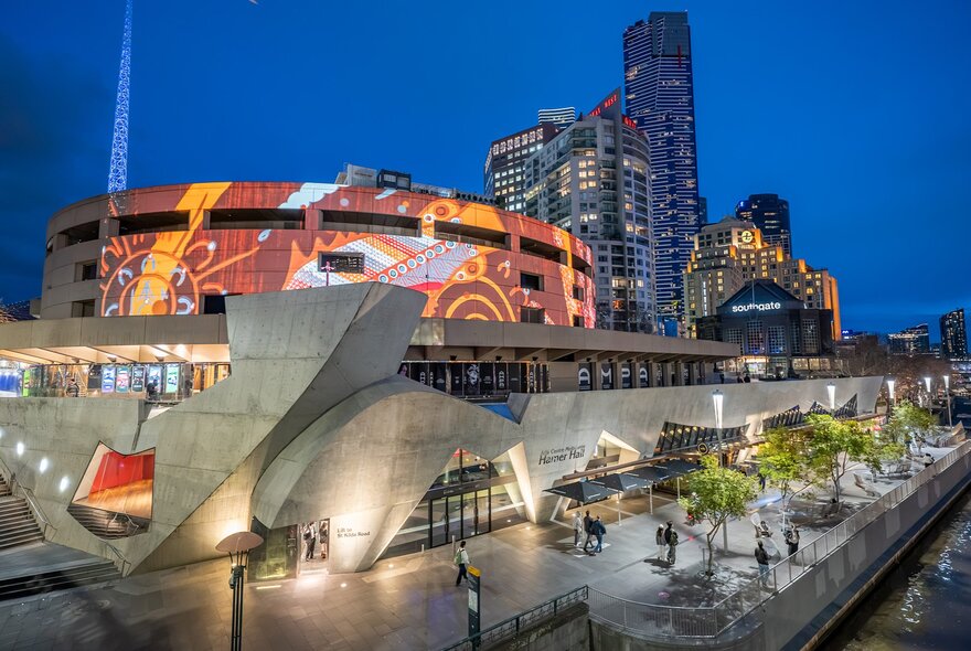 The Arts Centre illuminated at night with city buildings in the background.