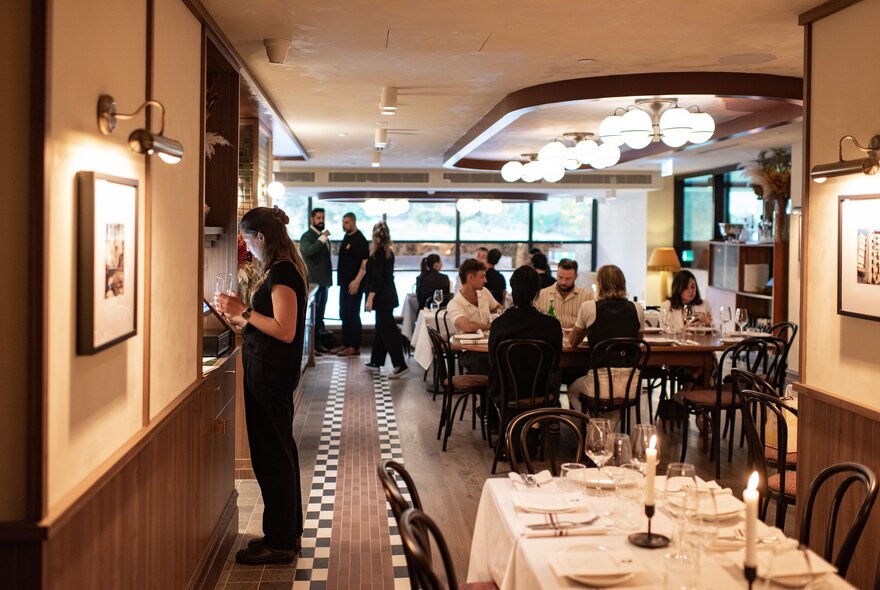 Restaurant interior with large tables, overhead lights and staff at pass.