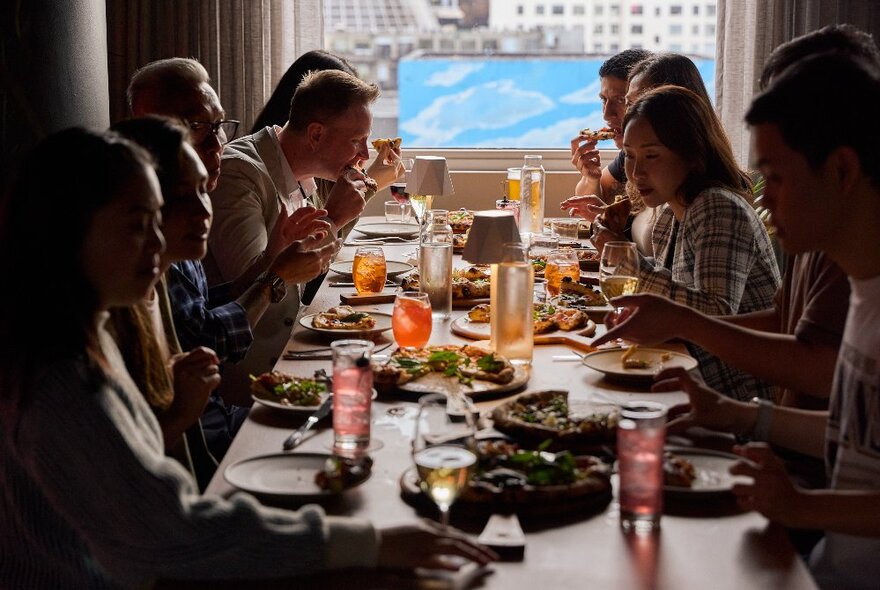 A long table with people seated eating, drinking and chatting.