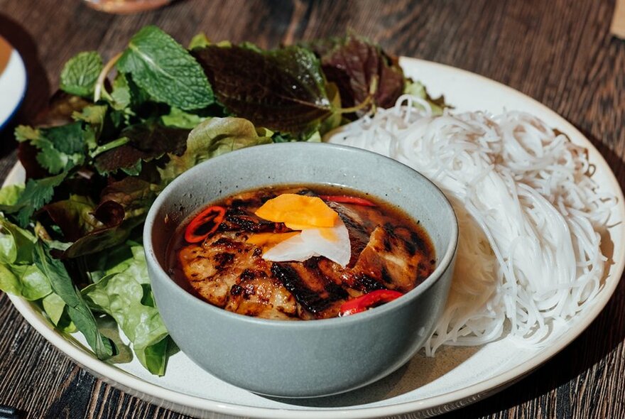 A platter with salad leaves, noodles and a bowl of food topped with an egg.