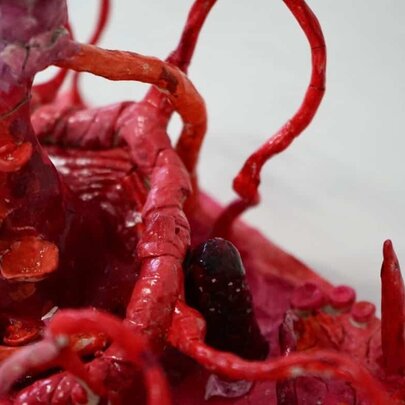 An organic clay sculpture that resembles red tendrils, blood vessels or roots.