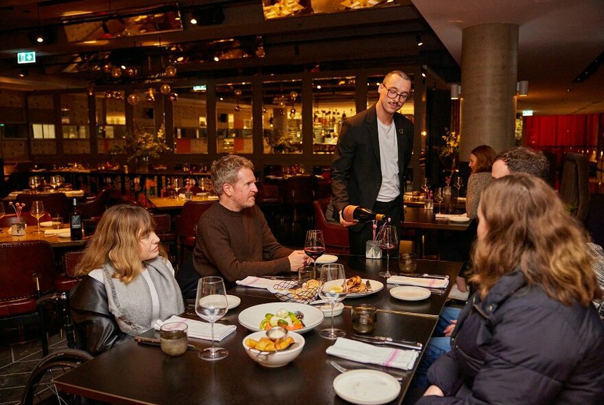 A waiter pouring wine for guests in a restaurant.