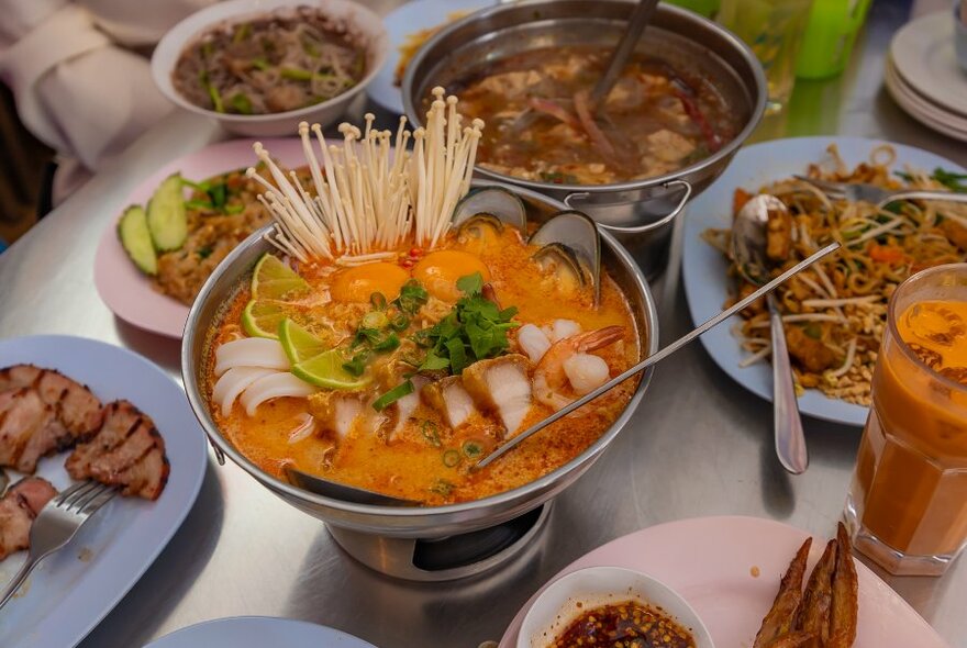 A table of Thai food including hot pot, noodles and soup.