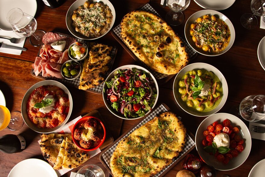 Looking down on a table with a vast array of pizza and salads.
