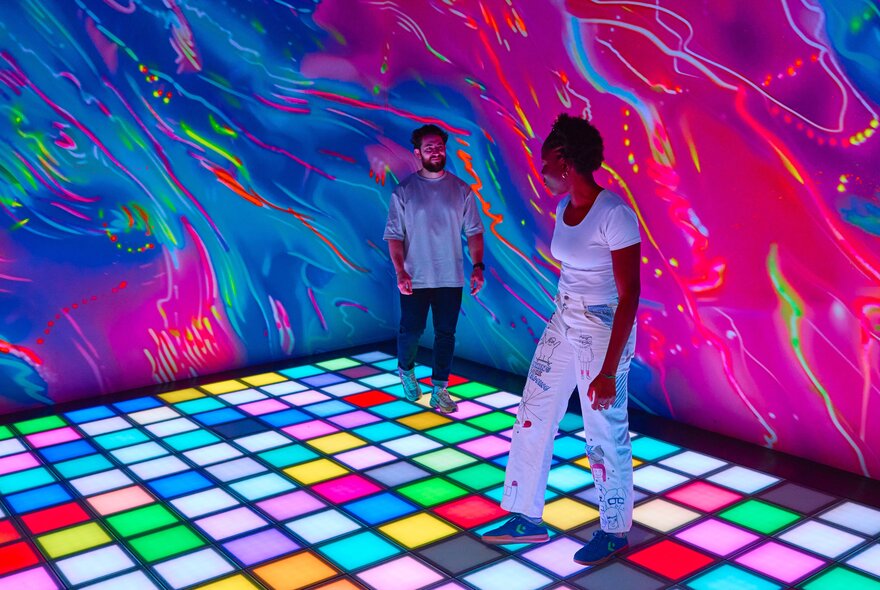 A man and a woman in a colourful room with light up multicolour tiles on the floor.