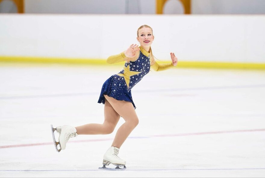 A young skater in a dress with starts on it performs on the ice.