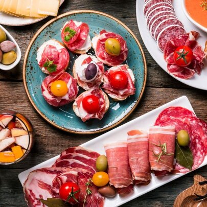 Plates of delicious looking smoked meats, olives, bread and tomatoes.