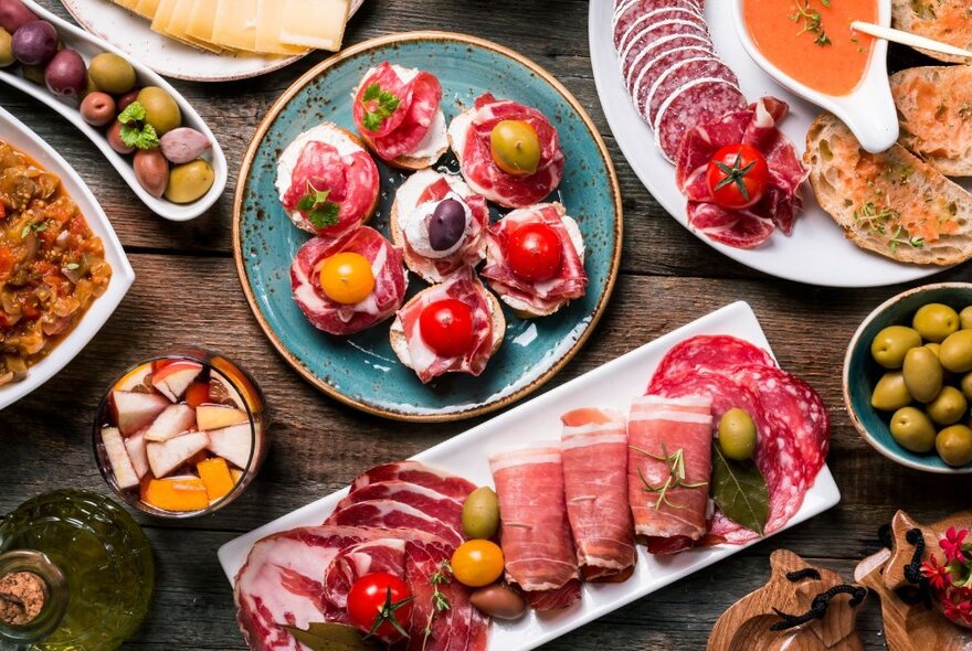 Plates of delicious looking smoked meats, olives, bread and tomatoes.