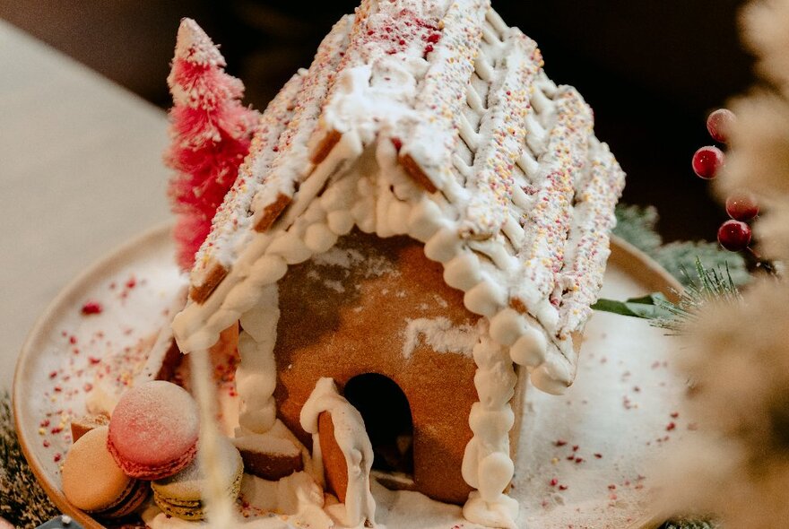 A festive gingerbread house, covered in snow,  on a plate.