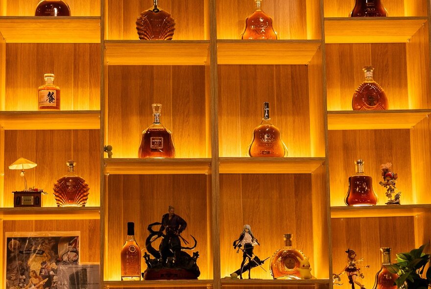 Japanese-styled illuminated wooden wall niches, each holding a decoration including bottles of spirits and ornaments.