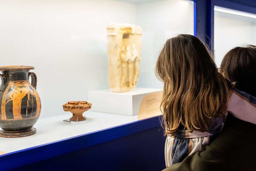 Person looking at Ancient Greek vases and objects in a display case.