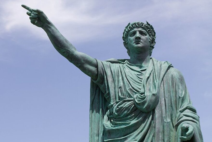A Roman statue of a man in a toga with his hand pointing towards the sky. 