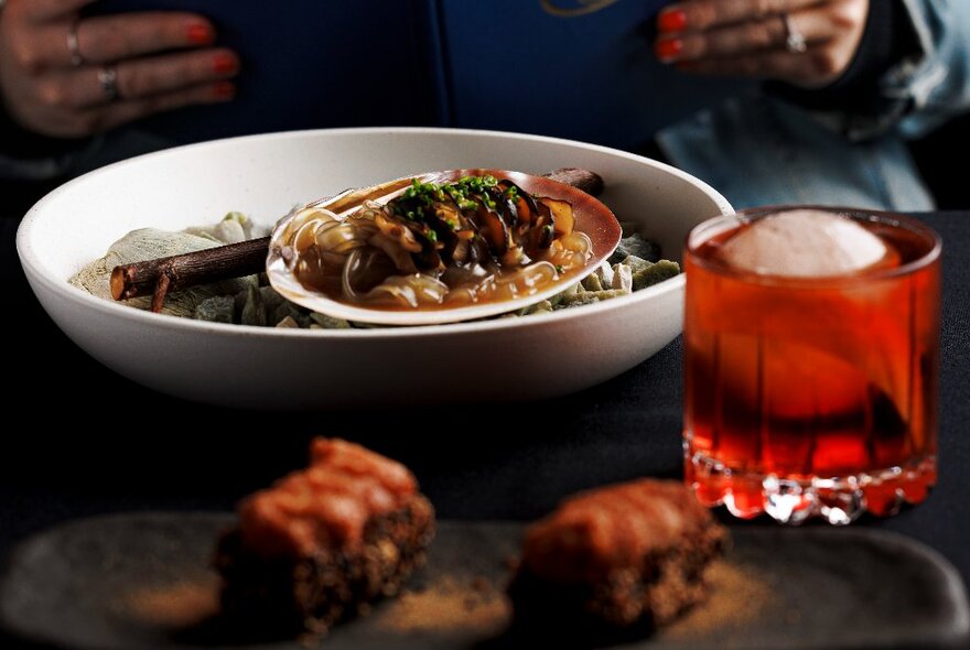 Dishes of Asian food on a dark table with a red iced drink.
