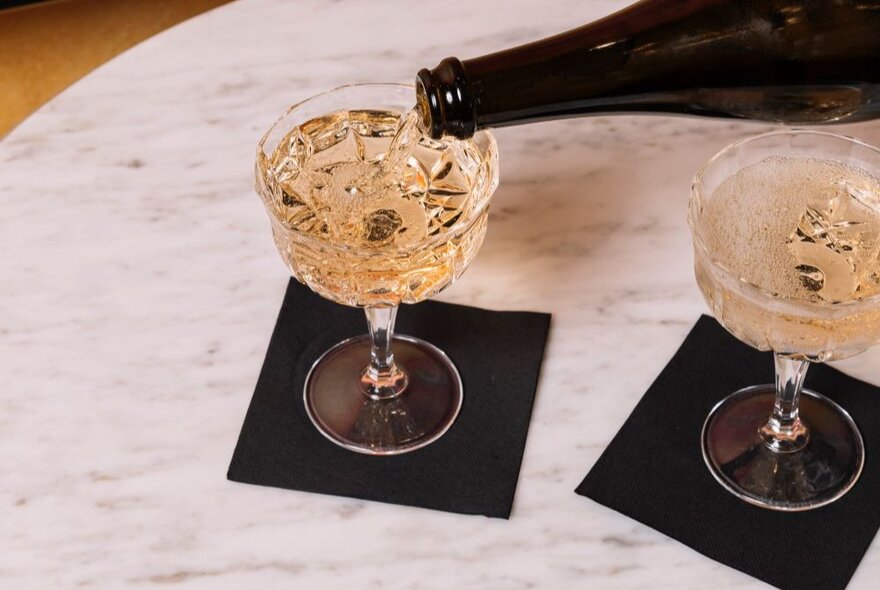Sparkling wine being poured from a bottle into two glasses.