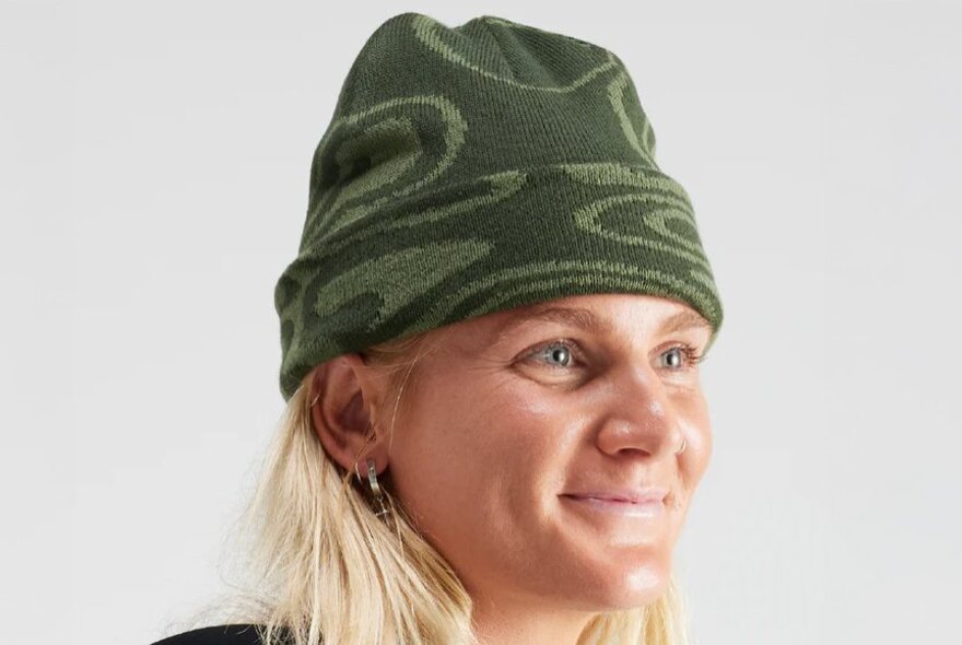A model wearing a green beanie high on her head with a cuff and swirling green patterns.