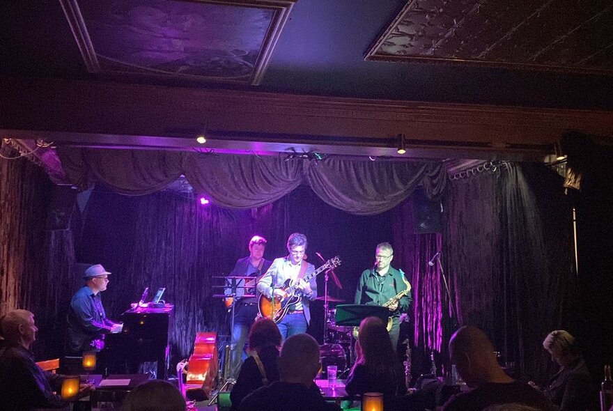 Band playing an intimate music venue with purple lighting and curtains.