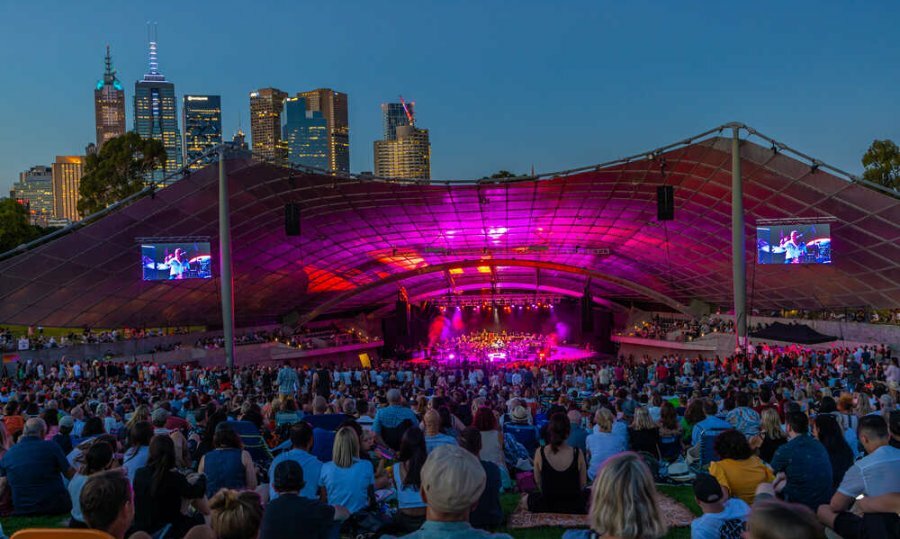 An outdoor stage at night with a crowd of people sitting in front of it