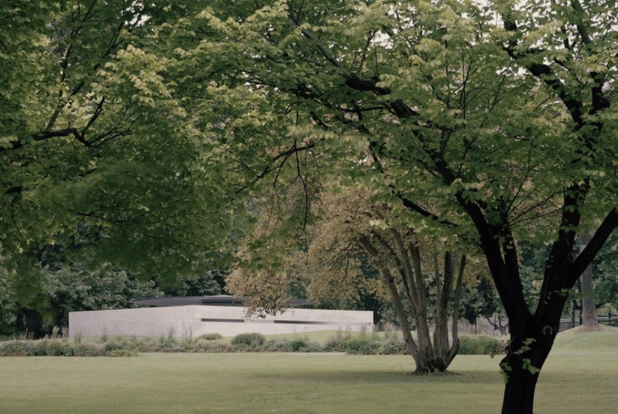 A view through parkland and trees to MPavilion, a low, concrete structure. 