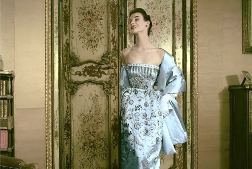 A beautiful woman modelling a luxurious pale blue silk Dior gown and shawl, in an opulent Paris apartment.