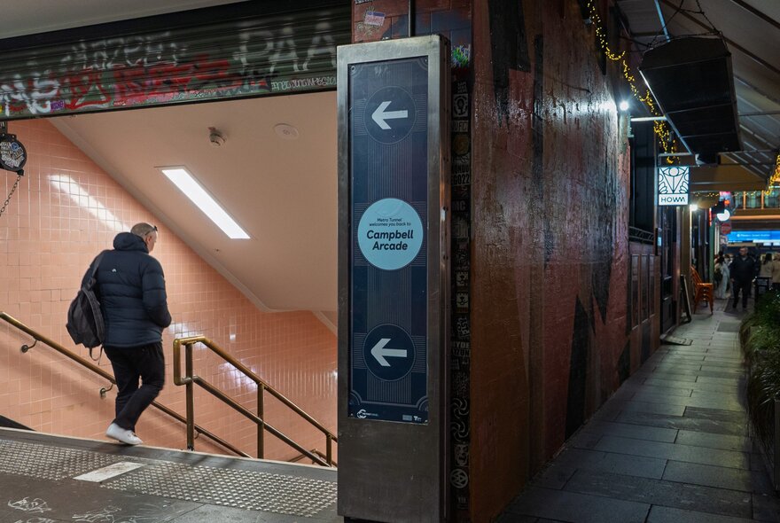 A man is walking downstairs into a pedestrian arcade underground. There are pink tiles on the wall.