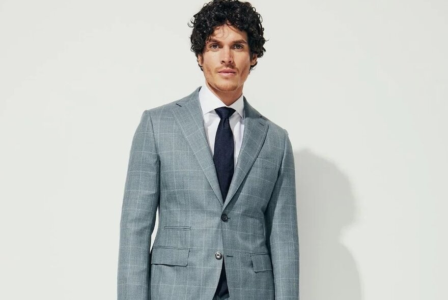 A male model wearing a tailored suit jacket in a very fine checked grey pattern.