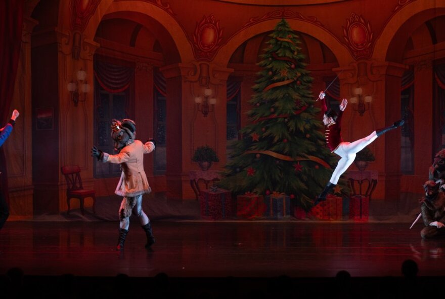 Two ballet dancers in costume dancing on a large stage, a Christmas tree in the background.