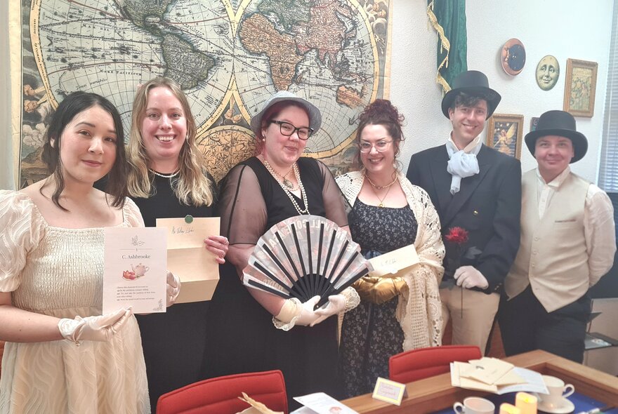 A group of women and men in Regency-era themed costumes standing in front of a vintage world map.