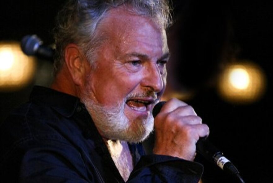 Australian musician, Ross Wilson, holding a microphone while singing on stage.