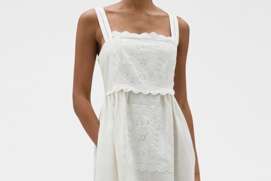 A model wearing a white dress with embroidered lace patches on it.