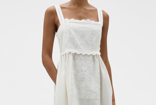 A model wearing a white dress with embroidered lace patches on it.