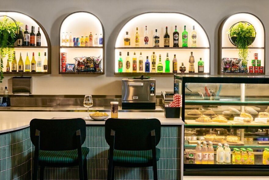 Bar counter with bar seats, glass food cabinet and backlit shelves lined with bottles.