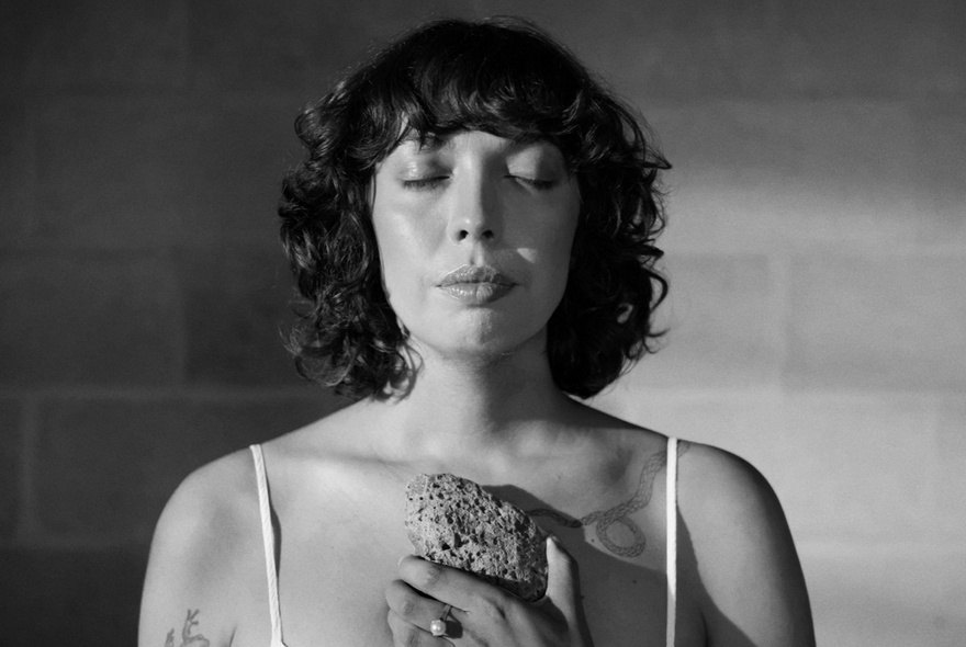 Still from the film, Eternity the Butterfly, showing a woman with black curly hair, eyes closed, holding a rock to her chest.