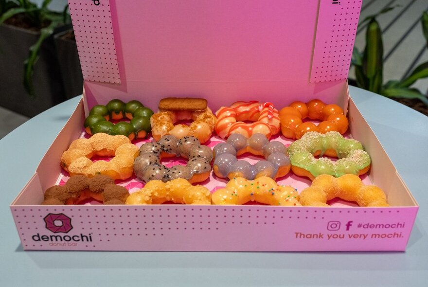 A pink box with mochi doughnuts covered in different coloured glazes.