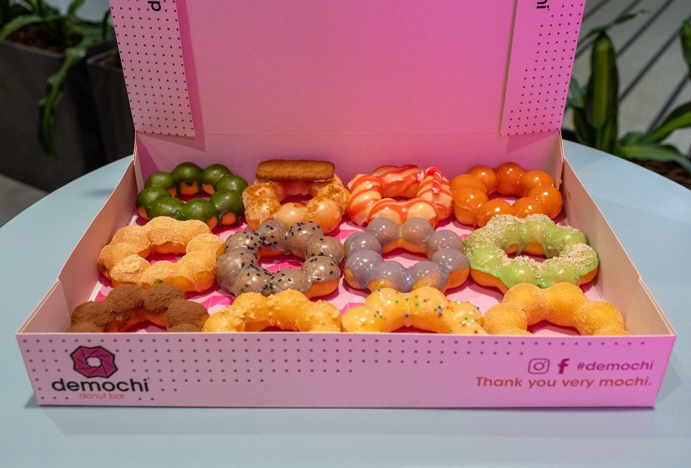 A pink box with mochi doughnuts covered in different coloured glazes.