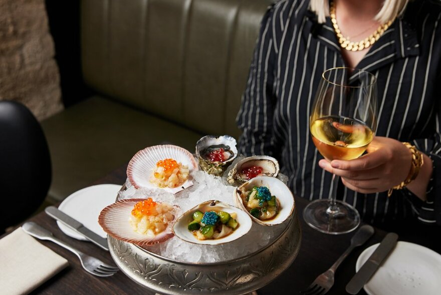 A woman is drinking a glass of wine and eating oysters and scallops