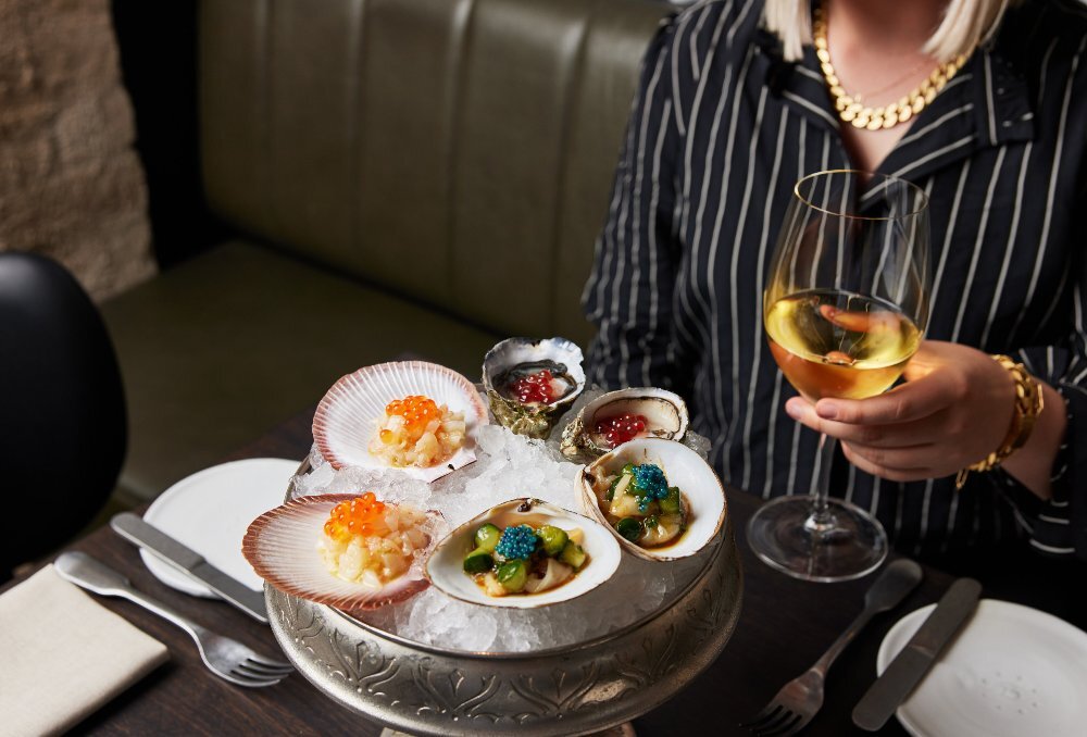 A woman is drinking a glass of wine and eating oysters and scallops