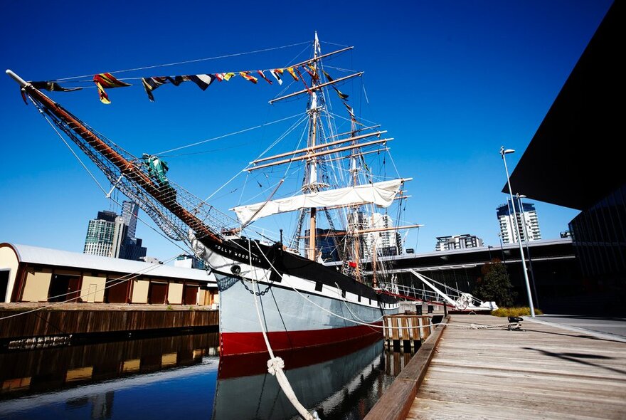 An old sailing ship with bunting moored at a pier.