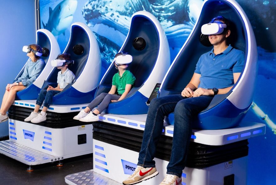 Two adults and two children seated in virtual reality pods with VR headsets on at the Melbourne Aquarium.