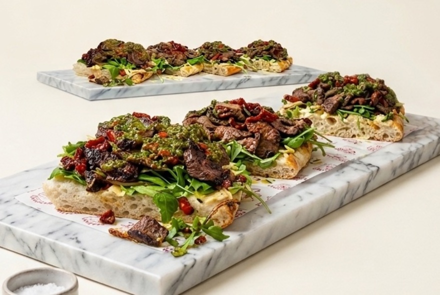 Meat heaped onto toasted bread with salad, on marble platters.